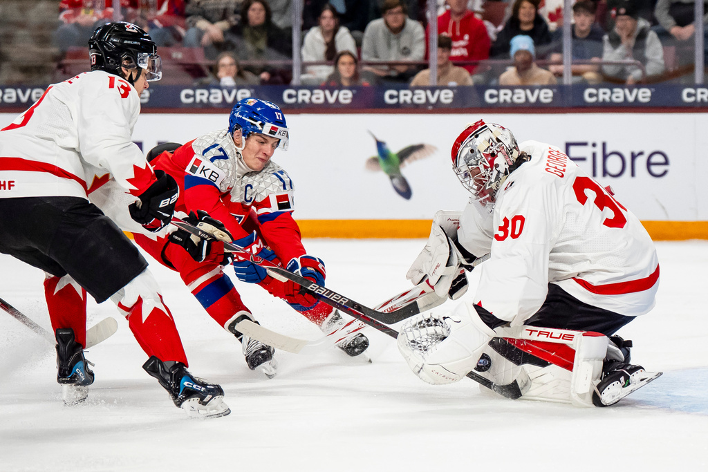 Canada goaltender Carter George makes a save on Czechia's Petr Sikora while Canada's Ethan MacKenzie, right, defends, during the first period of an IIHF World Junior Hockey Championship game in Minneapolis, Friday, Dec. 26, 2025. (Christopher Katsarov/The Canadian Press via AP)