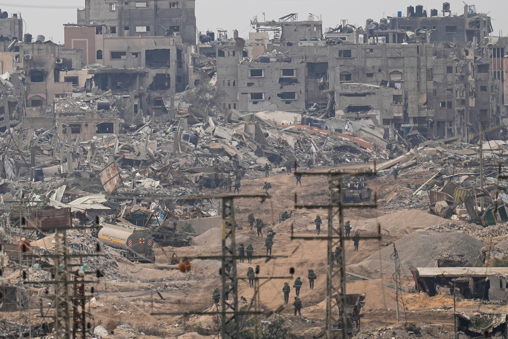 Israeli troops walk through the Gaza Strip as seen from southern Israel, Thursday, Dec. 21, 2023. (AP Photo/Ohad Zwigenberg)