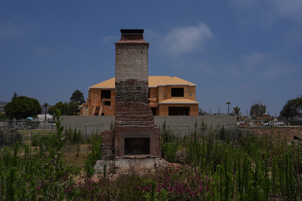 A chimney stands on a lot covered with weeds and wildflowers in front of a home under construction more than a year after the Palisades Fire in the Pacific Palisades neighborhood of Los Angeles, Thursday, June 4, 2026. (AP Photo/Jae C. Hong)