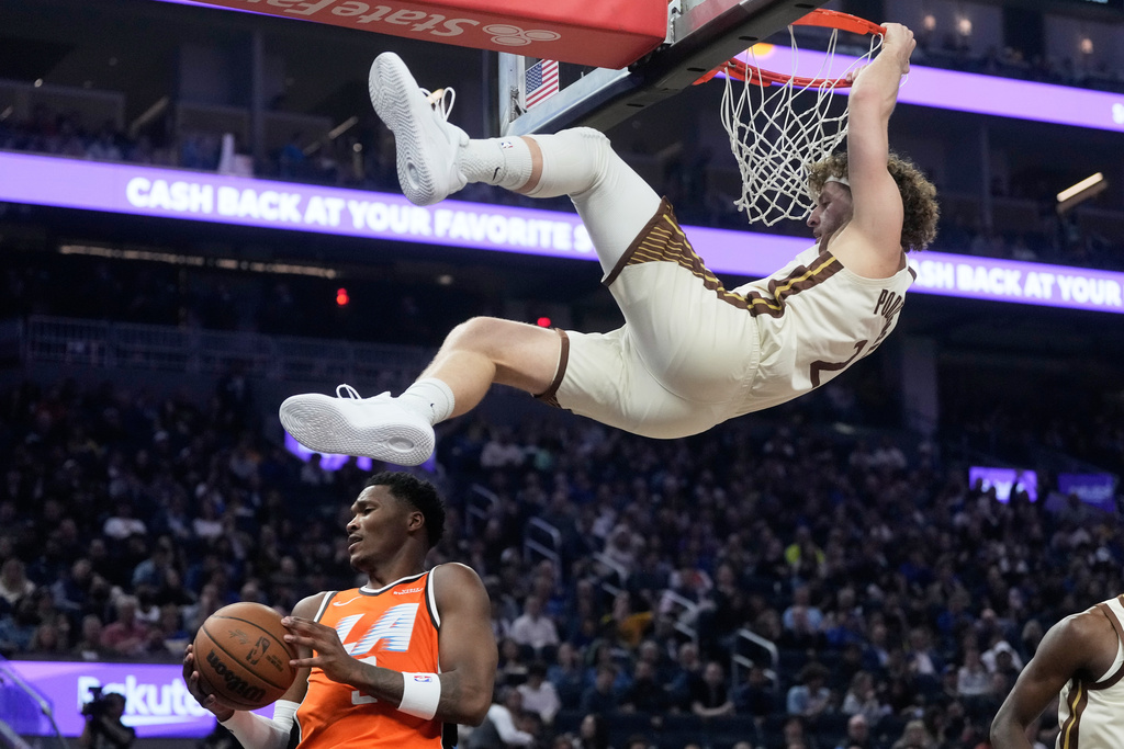 Golden State Warriors guard Brandin Podziemski, top, hangs onto the rim over Los Angeles Clippers guard Bennedict Mathurin after dunking during the first half of an NBA basketball game in San Francisco, Monday, March 2, 2026. (AP Photo/Jeff Chiu)