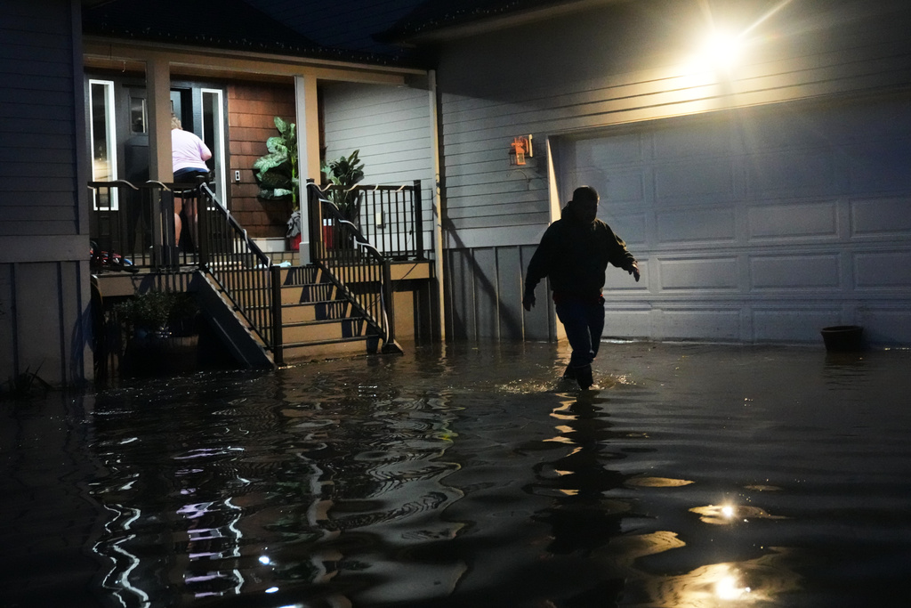 Haji Higa, right, and Lydia Heglin, left, walk through floodwaters at their front door after heavy rains led to historic flooding in the region Saturday, Dec. 13, 2025, in Burlington, Wash. (AP Photo/Lindsey Wasson)