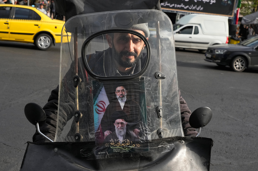 A man drives his motorbike with a poster on its windshield depicting Iran's Supreme Leader Ayatollah Mojtaba Khamenei, top, and his father, the slain Supreme Leader Ayatollah Ali Khamenei, who was killed in the U.S. and Israel strikes on Feb. 28, in downtown Tehran, Iran, Monday, April 13, 2026. (AP Photo/Vahid Salemi)