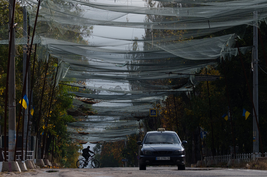 A local man rides a bicycle beneath anti-drone nets stretched over a street during a local ceasefire related to a humanitarian aid mission in Oleshky, in Kherson, Ukraine, Wednesday, Oct. 28, 2026. (AP Photo/Evgeniy Maloletka)