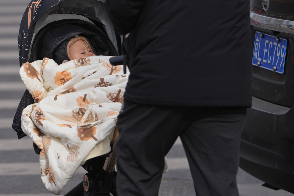 A man pushes a toddler on a stroller along a street in Beijing, Monday, Jan. 19, 2026. (AP Photo/Andy Wong)
