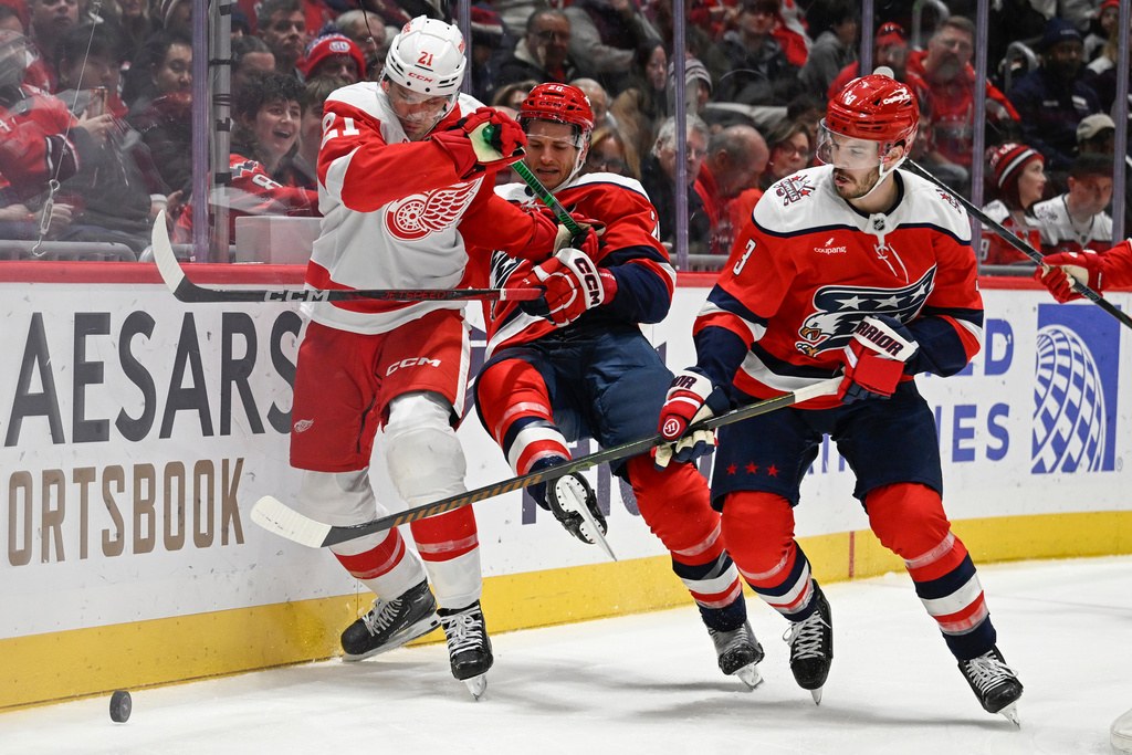 Washington Capitals defenseman Matt Roy, right moves in to gather the puck as Detroit Red Wings left wing James van Riemsdyk, left, knocks Capitals center Nic Dowd to the ice during the second period of an NHL hockey game, Saturday, Dec. 20, 2025, in Washington. (AP Photo/John McDonnell)