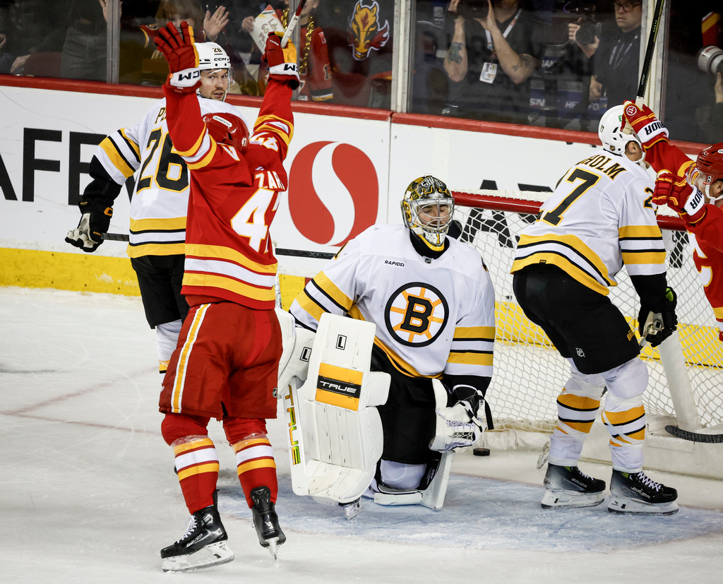 Boston Bruins goalie Jeremy Swayman, center, reacts as Calgary Flames' Connor Zary, front left, celebrates after his team's winning goal during overtime NHL hockey game action in Calgary, Alberta, Monday, Dec. 29, 2025. (Jeff McIntosh/The Canadian Press via AP)
