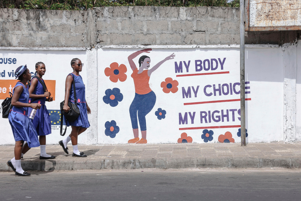 FILE - Schoolgirls walk home past a mural from the women's organization Plan International in Freetown, Sierra Leone, March 3, 2025. (AP Photo/Caitlin Kelly, File)