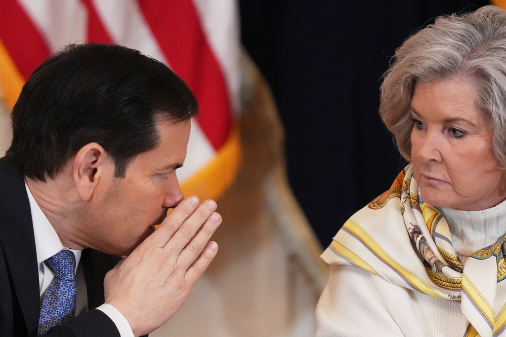 Secretary of State Marco Rubio, left, whispers to White House chief of staff Susie Wiles during a roundtable discussion on college sports in the East Room of the White House, Friday, March 6, 2026, in Washington. (AP Photo/Julia Demaree Nikhinson)