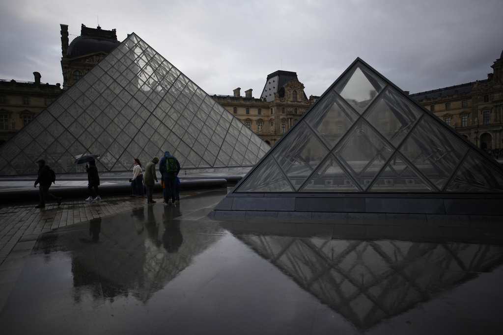 People tour the courtyard of Le Louvre museum in the rain Monday, Oct. 27, 2025 in Paris. (AP Photo/Christophe Ena)