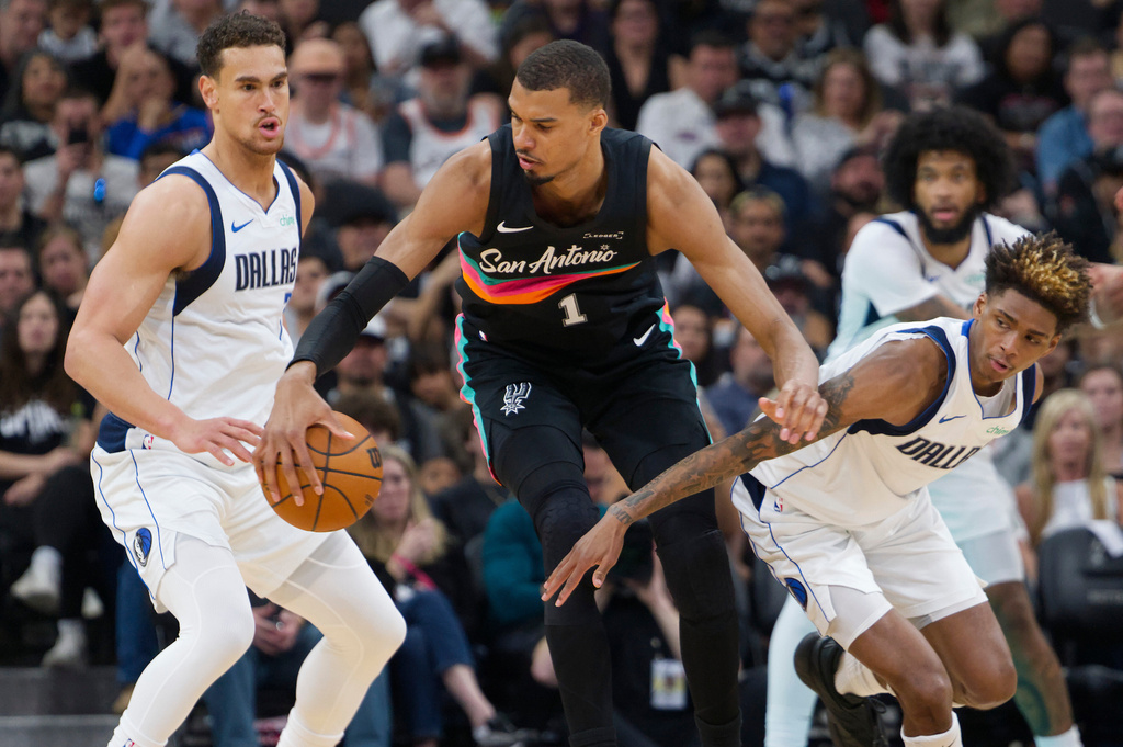 San Antonio Spurs center Victor Wembanyama (1) tangles with Dallas Mavericks' Dwight Powell, left, and A.J. Johnson during the first half of an NBA basketball game, Friday, April 10, 2026, in San Antonio. (AP Photo/Darren Abate)