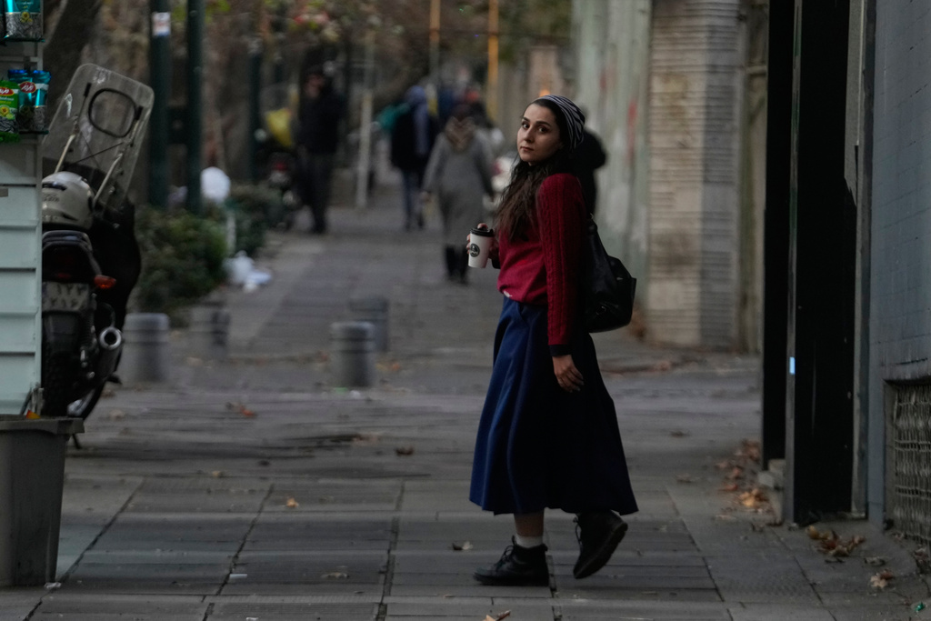 A woman holds her drink as she walks on a sidewalk in northern Tehran, Iran, Thursday, Nov. 20, 2025. (AP Photo/Vahid Salemi)