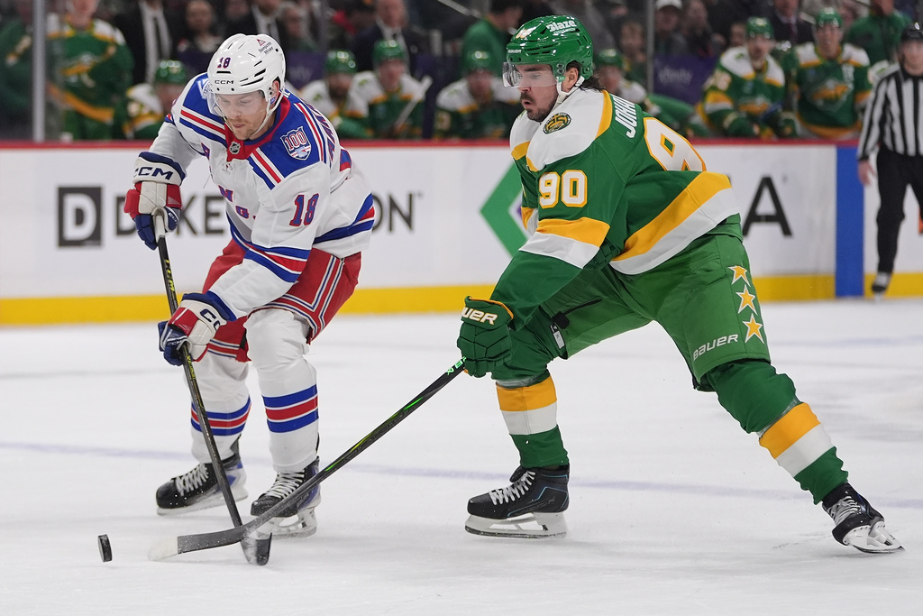 New York Rangers defenseman Urho Vaakanainen (18) and Minnesota Wild left wing Marcus Johansson (90) reach for the puck during the first period of an NHL hockey game, Saturday, March 14, 2026, in St. Paul, Minn. (AP Photo/Abbie Parr)