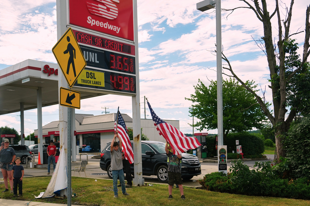 People hold flags in front of a gas station as President Donald Trump's motorcade passes by Tuesday, June 23, 2026, in Pennsylvania. (AP Photo/Julia Demaree Nikhinson)