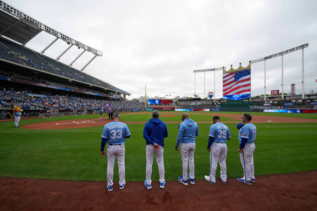 Coaches for the Kansas City Royals stand for the national anthem at Kauffman Stadium before a baseball game against the Baltimore Orioles, Wednesday, April 22, 2026, in Kansas City, Mo. (AP Photo/Charlie Riedel)