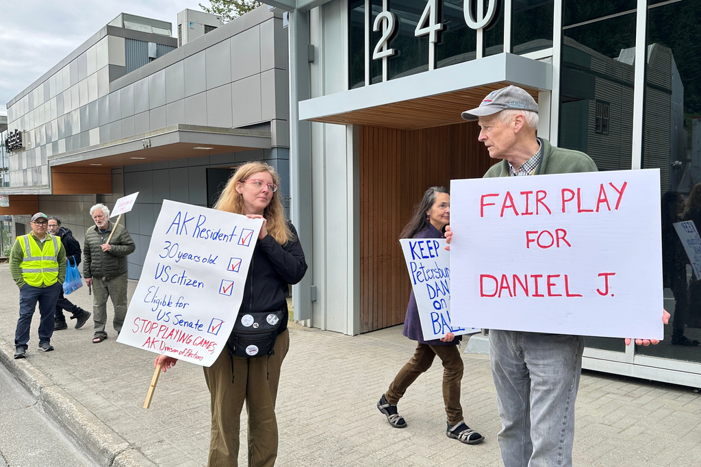 Anjuli Grantham, left, and Ben Muse protest with others outside the Alaska Division of Elections office on Friday, June 12, 2026, in Juneau, Alaska, opposing efforts to block from the ballot a U.S. Senate candidate who shares the same name and party affiliation as the incumbent Republican Dan Sullivan. (AP Photo/Becky Bohrer)