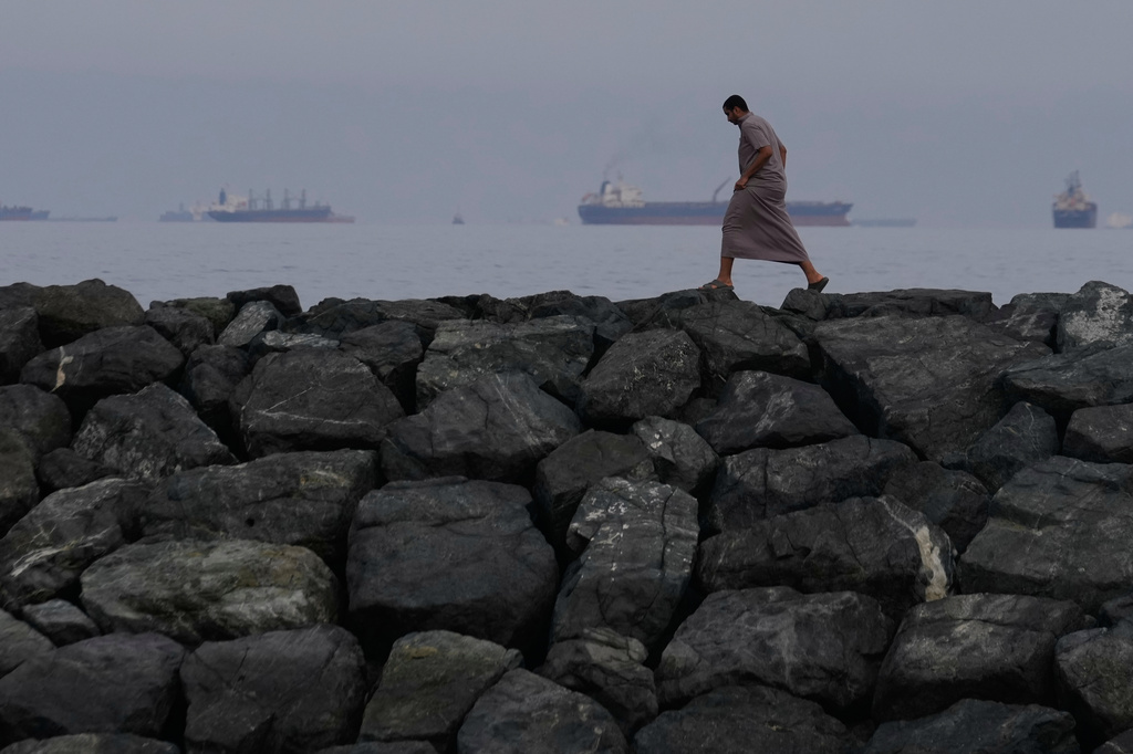 FILE- A man walks along the shore as oil tankers and cargo ships line up in the Strait of Hormuz, seen from Khor Fakkan, United Arab Emirates, March 11, 2026. (AP Photo/Altaf Qadri, File)