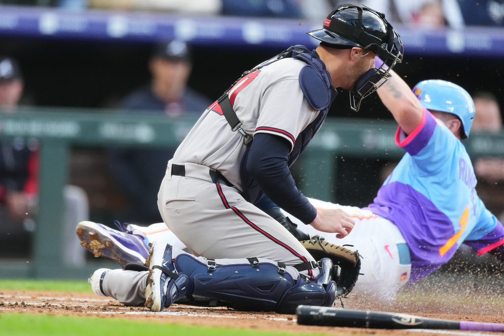 Atlanta Braves catcher Jonah Heim, front, tries to field the throw as Colorado Rockies' TJ Rumfield scores on a ground out by Willi Castro in the first inning of a baseball game Friday, May 1, 2026, in Denver. (AP Photo/David Zalubowski)