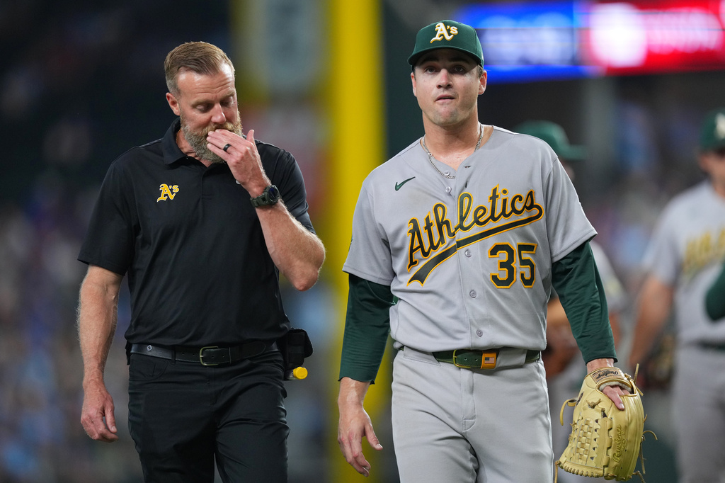 Athletics starting pitcher J.T. Ginn (35) leaves the field with head trainer Jeff Collins during the fourth inning of a baseball game against the Texas Rangers Sunday, April 26, 2026, in Arlington, Texas. (AP Photo/Julio Cortez)
