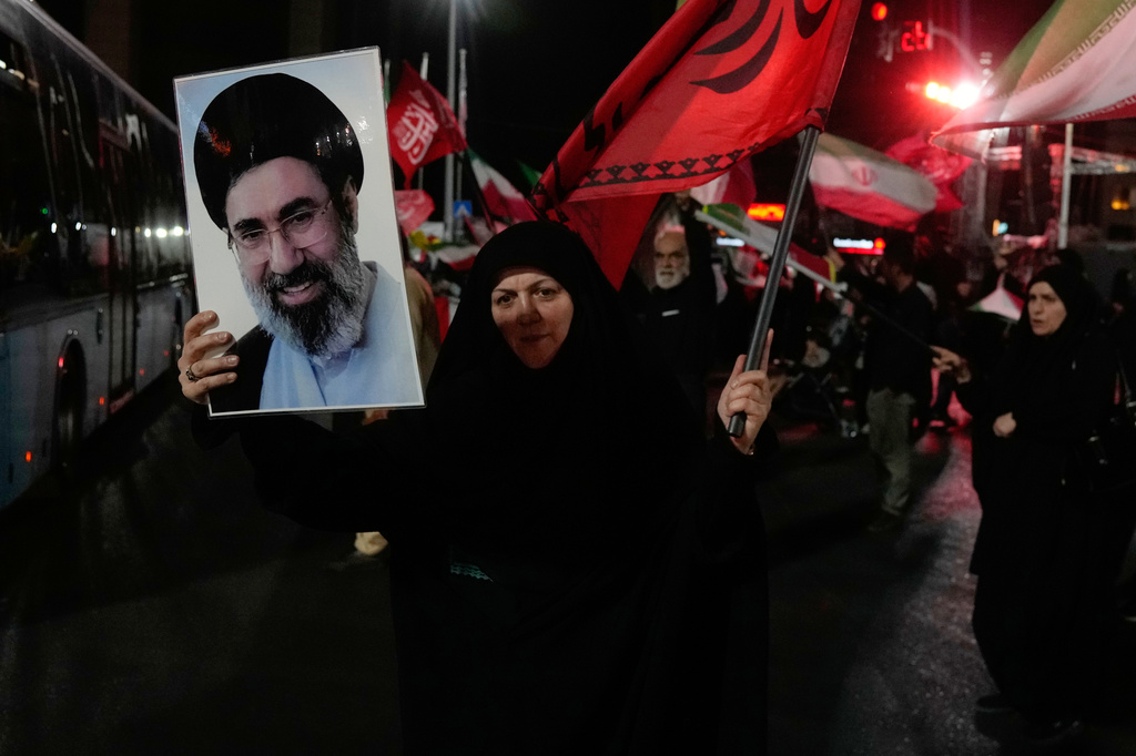 A woman holds up a poster of Iranian Supreme Leader Ayatollah Mojtaba Khamenei and waves a flag during a pro-government gathering at a square in Tehran, Iran, Tuesday, Aug. 11, 2026. (AP Photo/Vahid Salemi)
