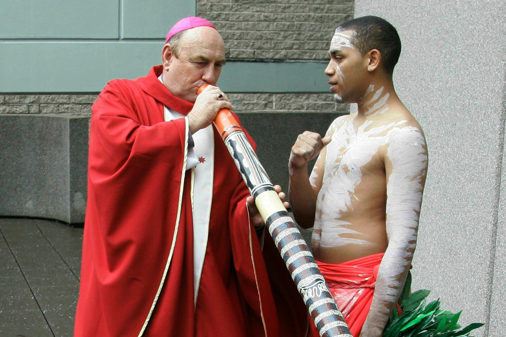 FILE - Bishop Christopher Saunders of Broome, left, tries to play a didgeridoo during a World Youth Day 2008 media event in Sydney, Australia, on April 17, 2008. (AP Photo/Rob Griffith, File)
