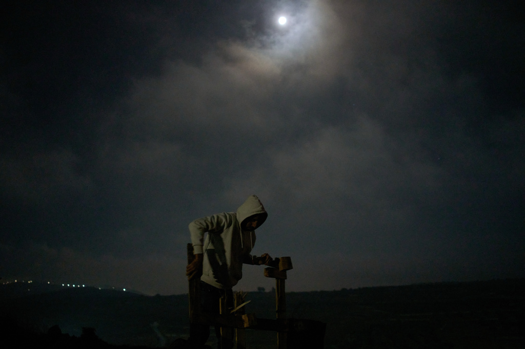 A Palestinian breaks apart a wooden pallet to fuel a bonfire during a volunteer night watch to help prevent Israeli settler attacks in the West Bank town of Sinjil, Monday, July 27, 2026. (AP Photo/Leo Correa)