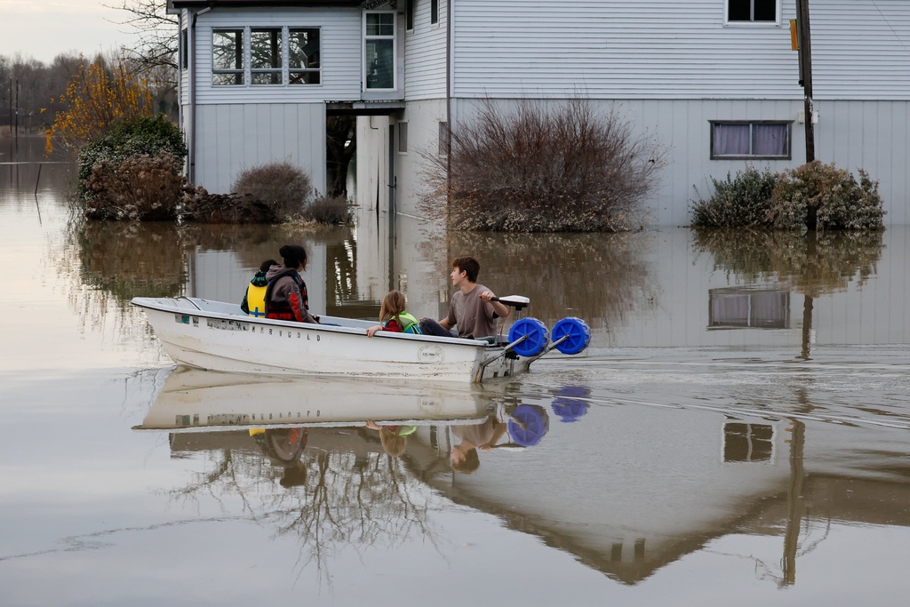 Carter Johnson, 16, uses a boat to transport his five-year-old brother, Milo, and two neighbors past a flooded house in what was their front yard Saturday, Dec. 13, 2025, near Clear Lake, Wash. (Jennifer Buchanan/The Seattle Times via AP)