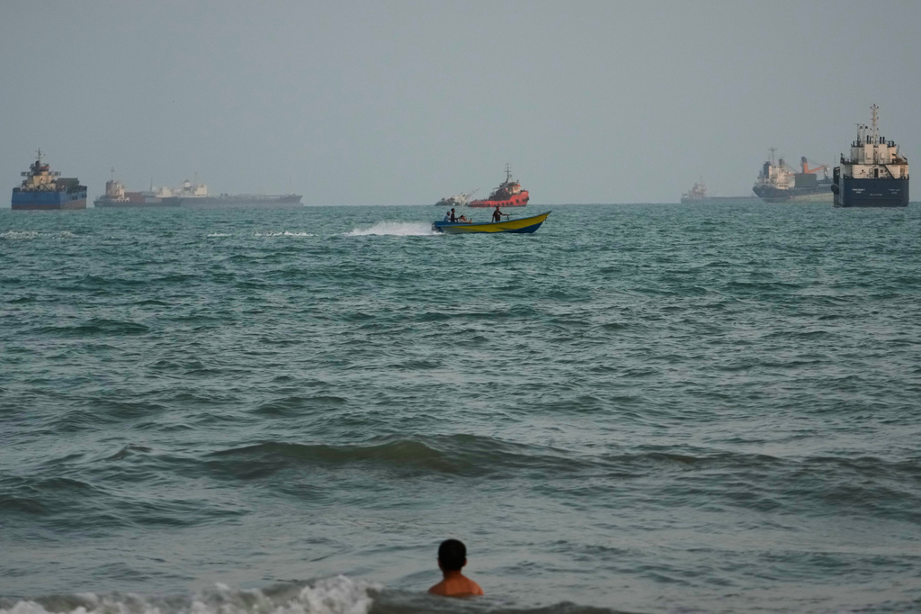 A swimmer remains near the shore as a motorboat passes commercial vessels anchored in the Strait of Hormuz off Bandar Abbas, Iran, Friday, Sept. 4, 2026. (AP Photo/Vahid Salemi)