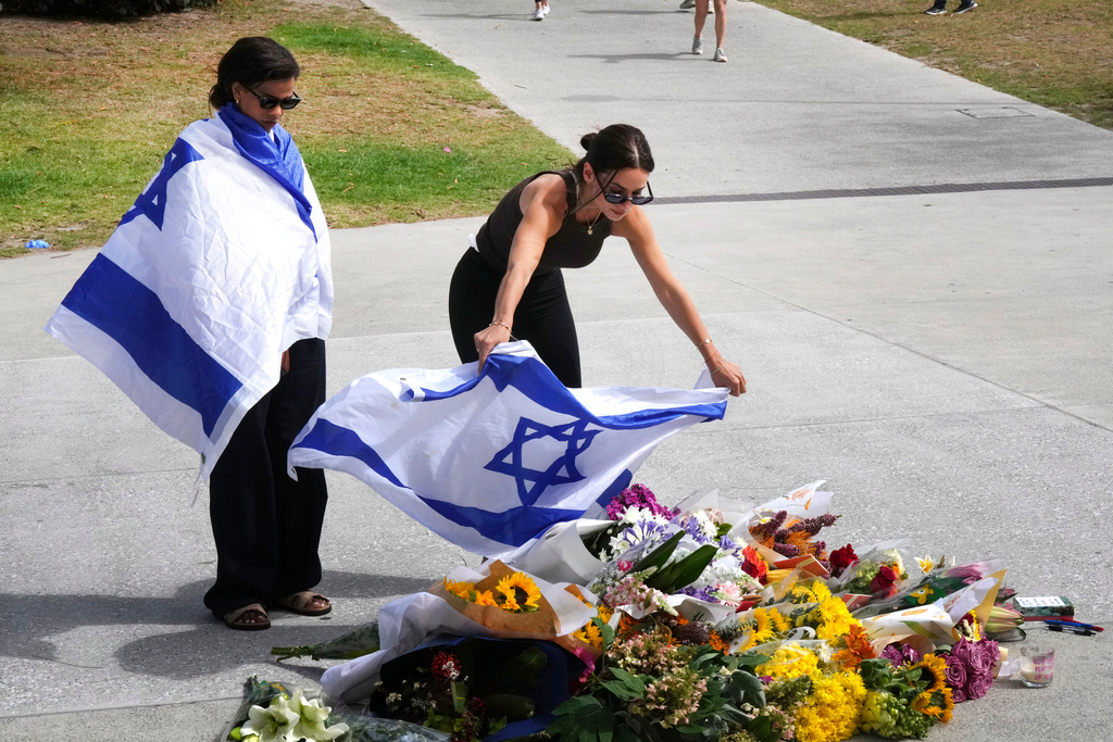 A woman places an Israeli flag over flowers outside Bondi Pavilion at Sydney's Bondi Beach, Monday, Dec. 15, 2025, a day after a shooting. (AP Photo/Mark Baker)