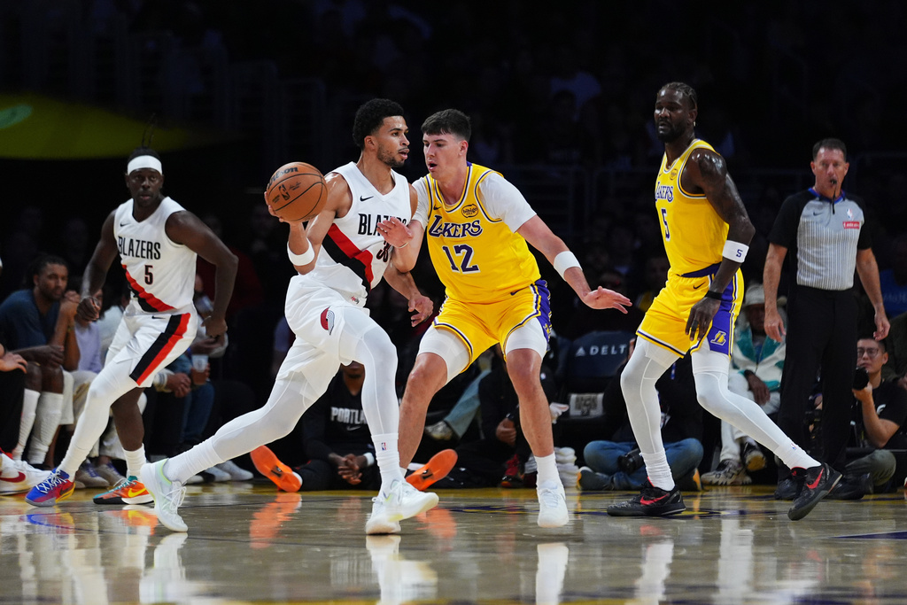 Portland Trail Blazers forward Toumani Camara, center left, is defended by Los Angeles Lakers forward Jake LaRavia (12) during the first half of an NBA basketball game Monday, Oct. 27, 2025, in Los Angeles. (AP Photo/Ethan Swope)