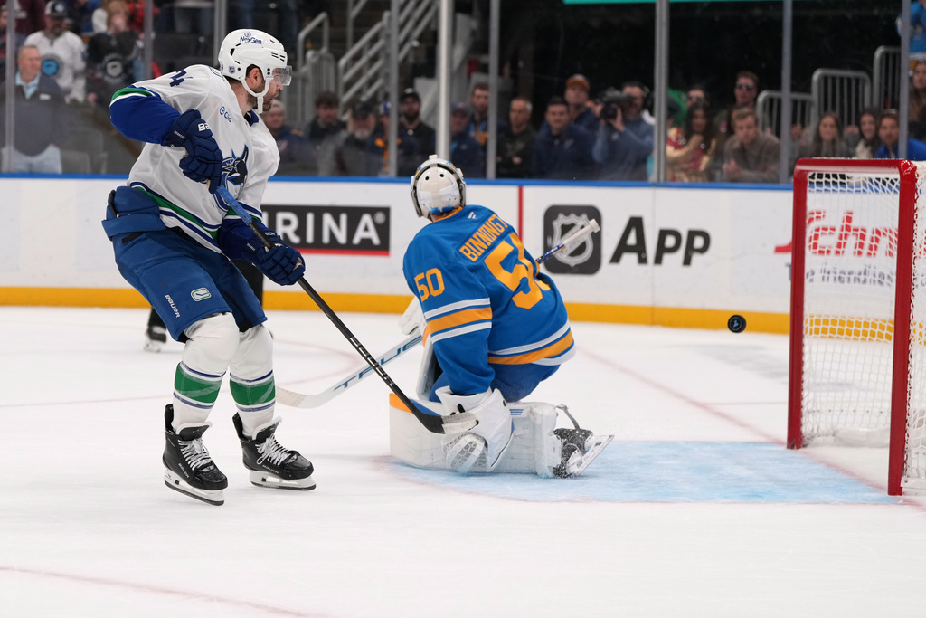 Vancouver Canucks' Jake DeBrusk, left, scores the game-winning goal past St. Louis Blues goaltender Jordan Binnington (50) in a shootout of an NHL hockey game Thursday, Oct. 30, 2025, in St. Louis. (AP Photo/Jeff Roberson)