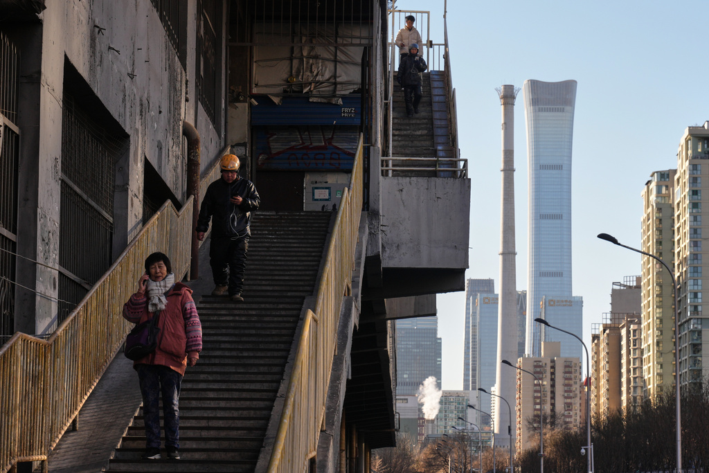 People walk down steps near a residential building area with a view of China Zun, the tallest skyscraper in Beijing, Tuesday, Dec. 23, 2025. (AP Photo/Andy Wong)