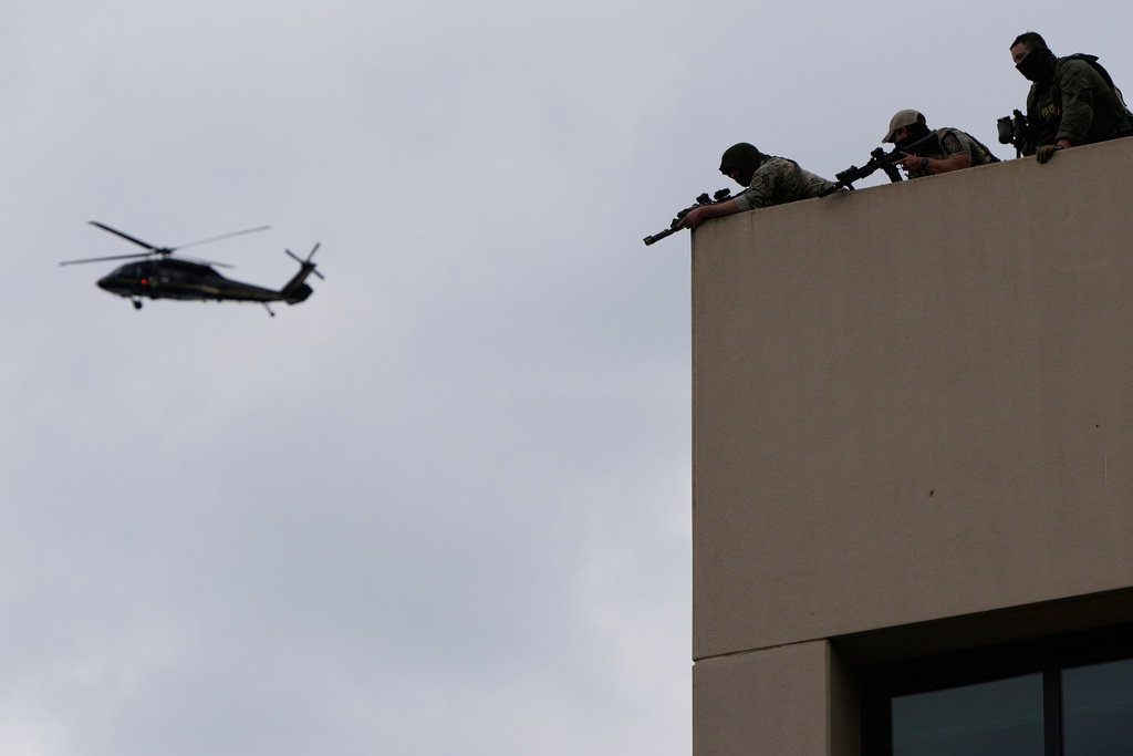 Law enforcement agents aim their weapons from the roof of a U.S. Immigration and Customs Enforcement facility as a helicopter flies past during a protest on Saturday, Oct. 4, 2025, in Portland, Ore. (AP Photo/Jenny Kane)