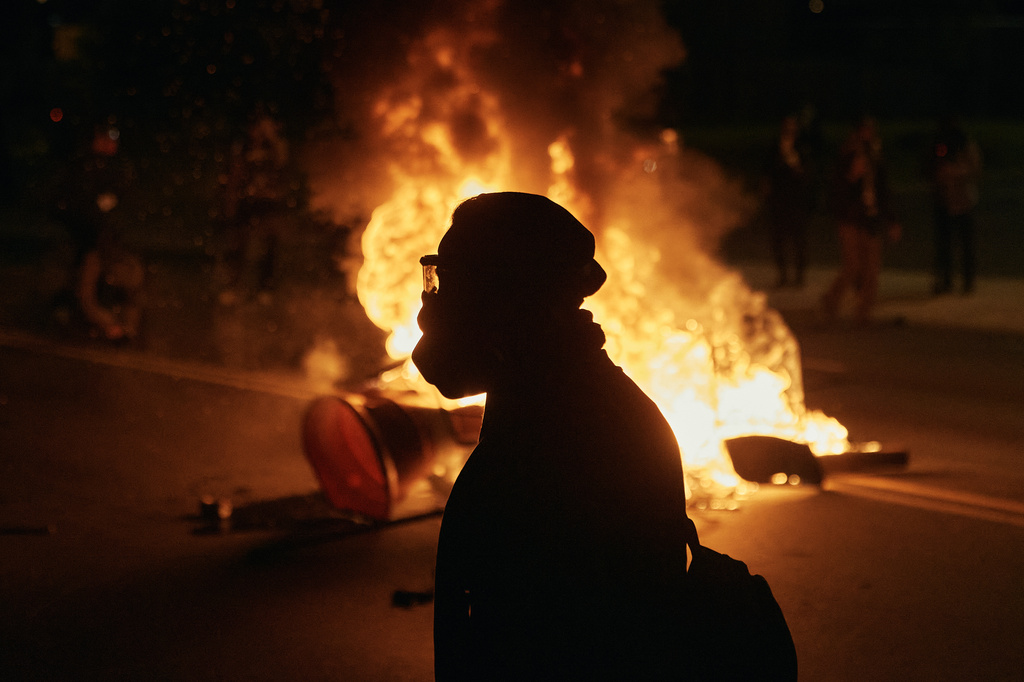 A man wearing protective gear walks in front of a burning barricade outside the Delaney Hall detention center during a protest against the transfer of detainees and federal immigration policies on Saturday, May 30, 2026, in Newark, N.J. (AP Photo/Andres Kudacki)