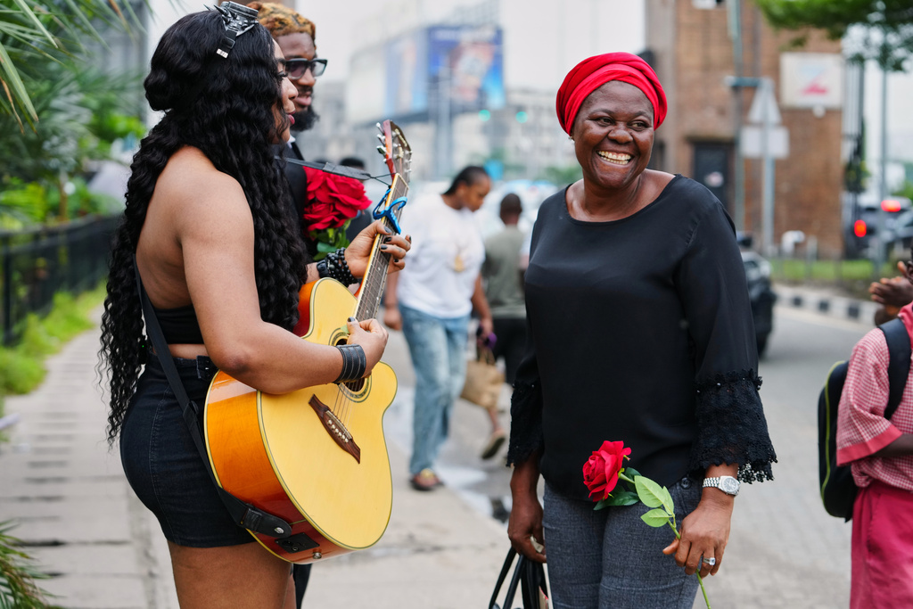 A commuter, right reacts as Nigerian rock musician Bianca "Clayrocksu" Okorocha, left, accompanied by Daniel Onyemachi-Chiweolu, popularly known as Machigold, behind, sings love songs handing single-stem roses to commuters ahead of Valentine's Day in Lagos, Nigeria, Tuesday, Feb.10, 2026. (AP Photo/Sunday Alamba)