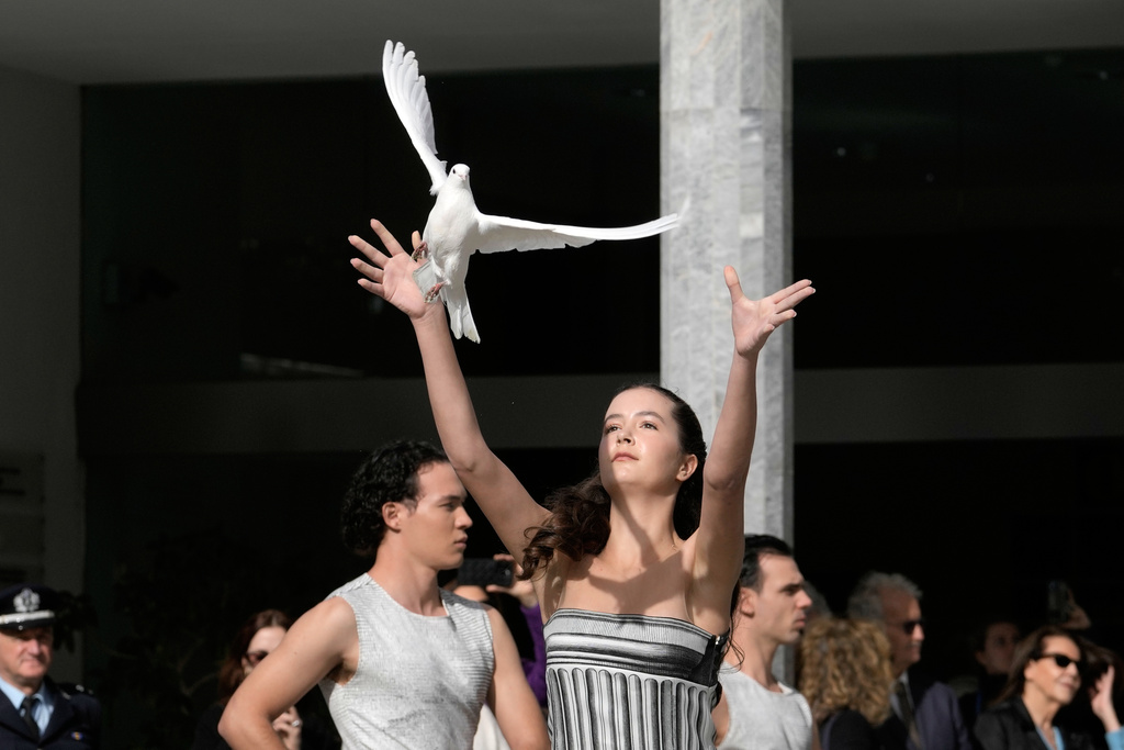 A girl releases a white pigeon during the start of the torch relay after the ceremony of the flame lighting for the Milan Cortina 2026 Winter Olympics, at the archaeological museum of Olympia, Greece, Wednesday, Nov. 26, 2025. (AP Photo/Petros Giannakouris)