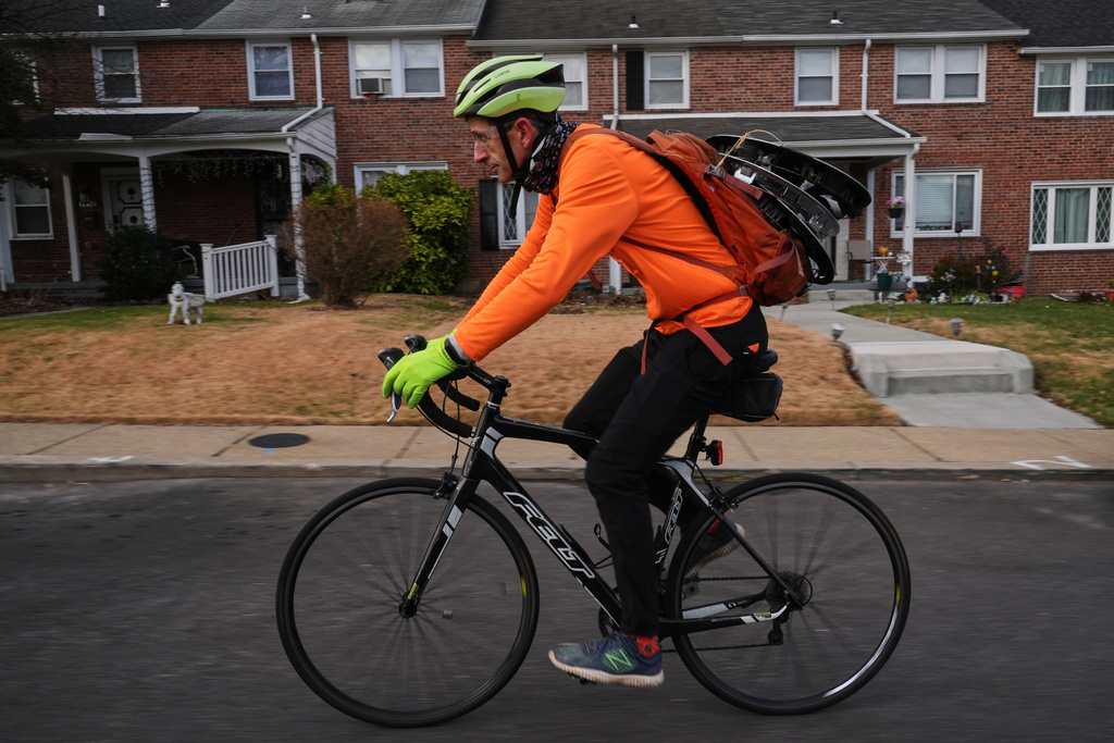 With hubcaps fastened to his backpack, cyclist Barnaby Wickham pedals through a neighborhood on his journey home, Thursday, Dec. 11, 2025, in Baltimore. (AP Photo/Stephanie Scarbrough)