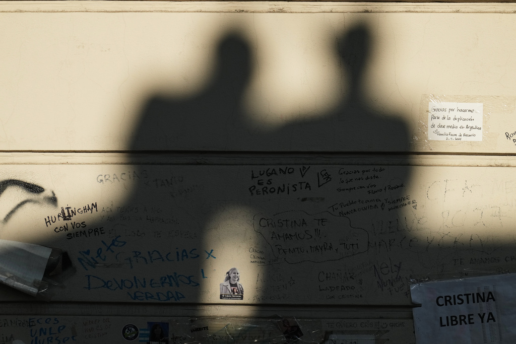 The shadows of supporters of Argentina's former President Cristina Fernandez are cast on her residential building, where she is currently serving a six-year house arrest sentence for corruption, on the day she is to appear in court for another trial for allegedly leading an illicit association, in Buenos Aires, Argentina, Tuesday, March 17, 2026. The sticker on the wall is of Argentina's late, first lady, Eva "Evita" Peron. (AP Photo/Natacha Pisarenko)