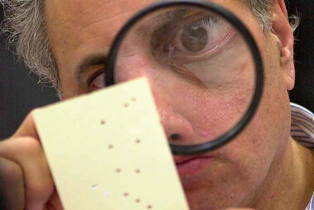 FILE - Broward County canvassing board member Judge Robert Rosenberg using a magnifying glass to examine a disputed ballot at the Broward County Courthouse in Fort Lauderdale, Fla., on Nov. 24, 2000. (AP Photo/Alan Diaz, File)