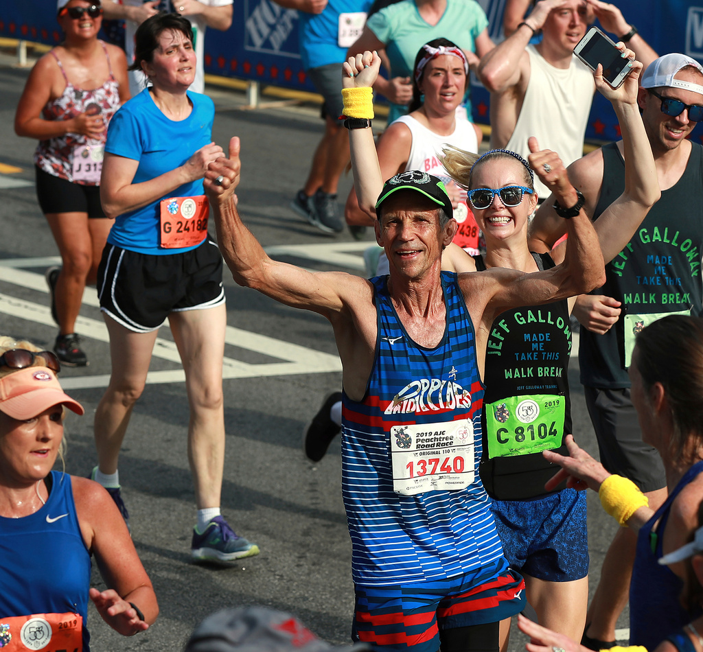 FILE - Jeff Galloway, the first winner of the race at its original running, gives a double thumbs up as he heads to the finish line in the 50th AJC Peachtree Road Race, Thursday, July 4, 2019, in Atlanta. (Curtis Compton//Atlanta Journal-Constitution via AP, File)