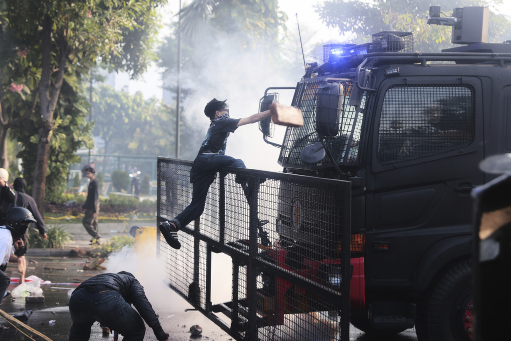 A man climbs on to a police water cannon truck during a protest following the death of a delivery rider in clashes between riot police and students protesting against lawmakers' allowances, in Surabaya, East Java, Indonesia, Friday, Aug. 29, 2025. (AP Photo/Trisnadi)