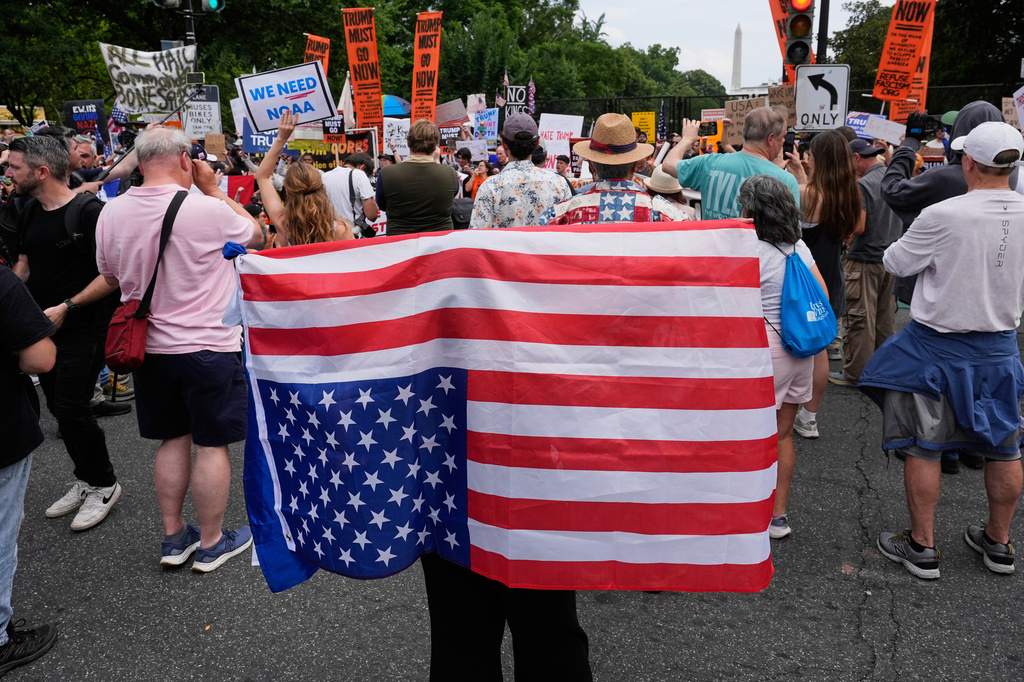 FILE - A demonstrator carries an American flag upside-down near the White House during a protest taking place on the day of a military parade commemorating the Army's 250th anniversary, coinciding with President Donald Trump's 79th birthday, June 14, 2025, in Washington. (AP Photo/Alex Brandon, File)