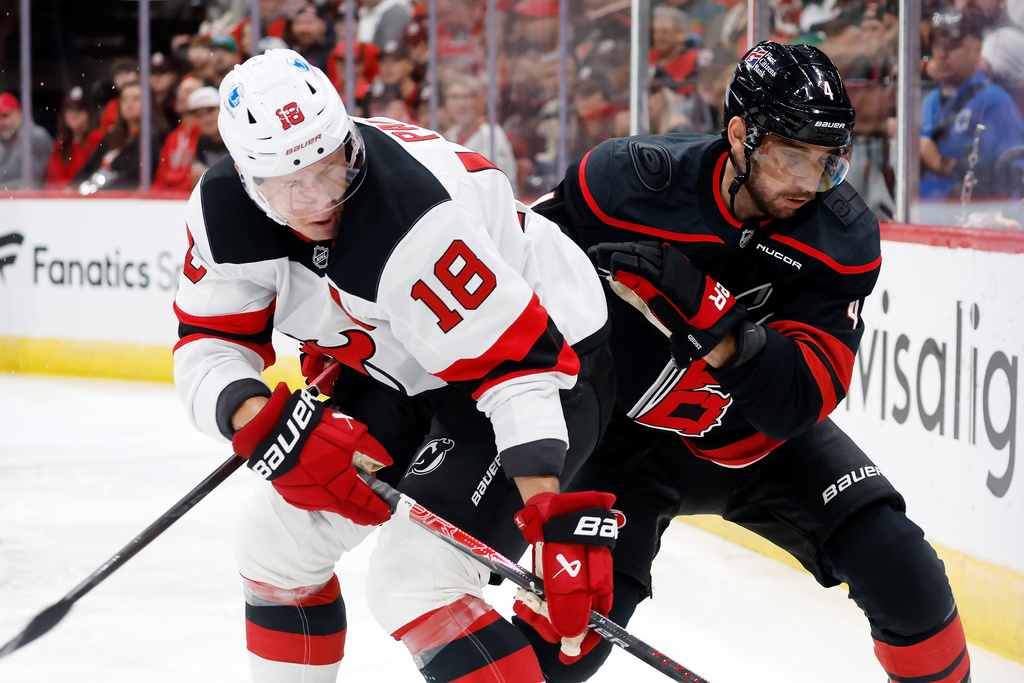 New Jersey Devils' Ondrej Palat (18) battles for the puck with Carolina Hurricanes' Shayne Gostisbehere (4) during the first period of an NHL hockey game in Raleigh, N.C., Thursday, Oct. 9, 2025. (AP Photo/Karl DeBlaker)