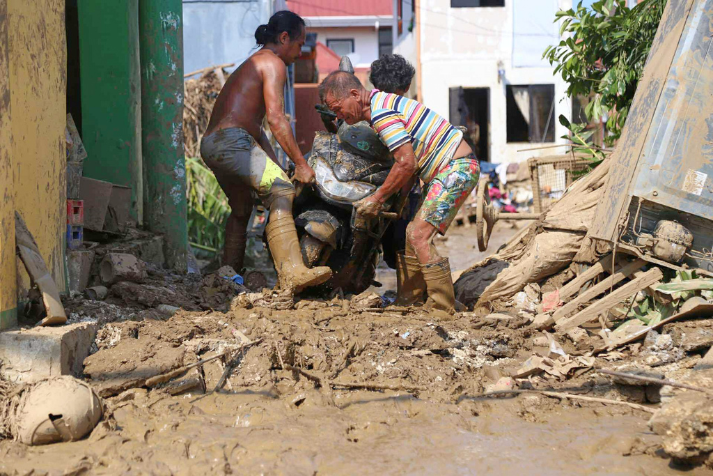 Residents carry a motorcycle along a muddied street caused by Typhoon Kalmaegi, in Liloan, Cebu province, central Philippines on Thursday, Nov.6, 2025. (AP Photo/Jacqueline Hernandez)