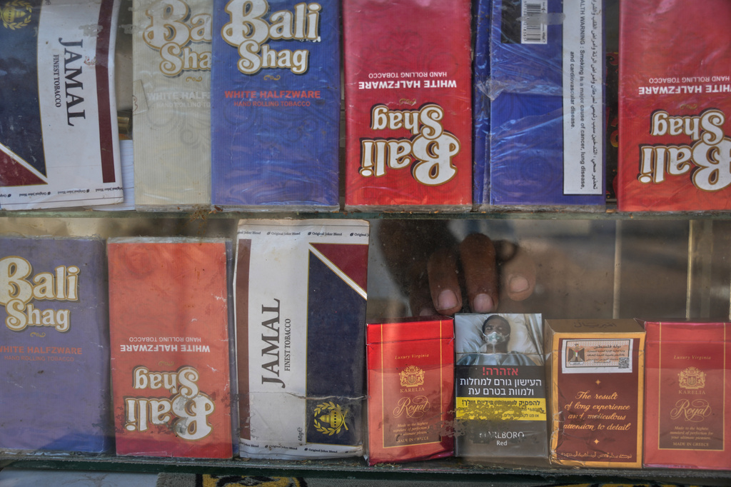 A vendor reaches for a pack of cigarettes at his kiosk in Deir al-Balah, central Gaza Strip, Friday, Aug 14, 2026. (AP Photo/Abdel Kareem Hana)