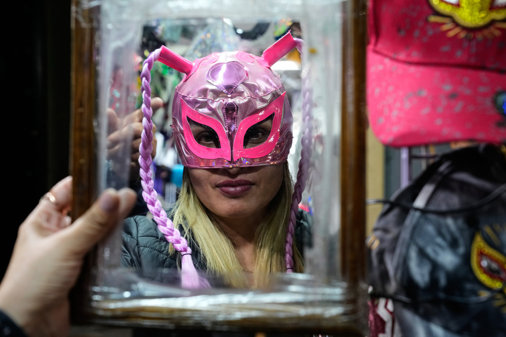 A Lucha fan looks in the mirror as she tries on a wrestling mask before entering Arena Mexico in Mexico City, Friday, June 26, 2026. (AP Photo/Marco Ugarte)