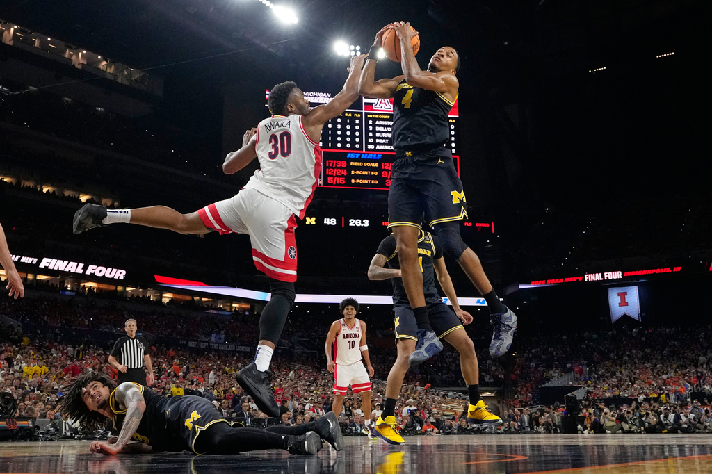 Michigan's Nimari Burnett (4) and Arizona's Tobe Awaka (30) reach for a rebound as Michigan's Elliot Cadeau, bottom, watches during the first half of an NCAA college basketball tournament semifinal game at the Final Four, Saturday, April 4, 2026, in Indianapolis. (AP Photo/Michael Conroy)