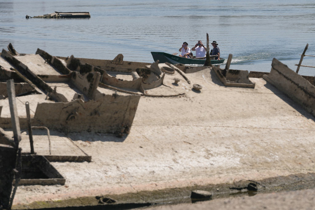 People watch the wreckage of a WWII German warship, emerged due to the drought, in front of Djerdap II, a large dam on the Danube River, between Romania and Serbia, near Prahovo, Serbia, Tuesday, Aug. 4, 2026. (AP Photo/Darko Vojinovic)