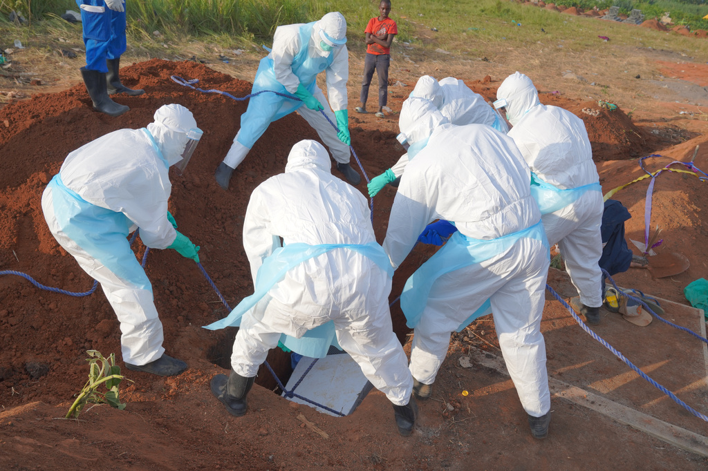 People dressed in protective gear lower into a grave the coffin containing the remains of Jacques Lobo Dhena, who died of Ebola, during a burial service in Bunia, Ituri province, eastern Congo, Wednesday, Aug. 12, 2026. (AP Photo/Dieudonne Dirole)