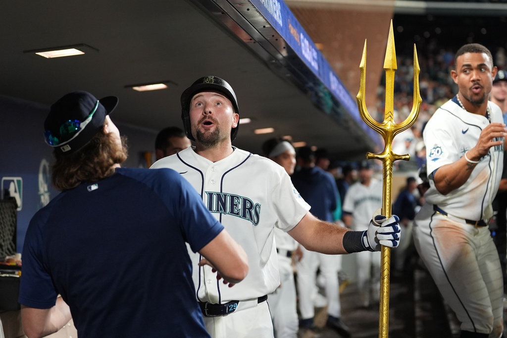 Seattle Mariners' Cal Raleigh, center, reacts after accidentally jumping into the ceiling of the dugout while celebrating his solo home run with pitcher Bryce Miller, left, during the seventh inning of a baseball game against the Philadelphia Phillies, Monday, Aug. 24, 2026, in Seattle. (AP Photo/Lindsey Wasson)