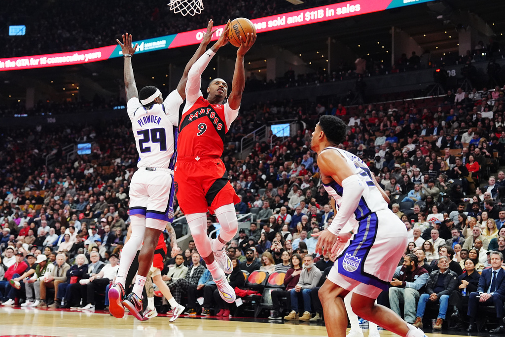 Toronto Raptors' RJ Barrett (9) leaps past Sacramento Kings' Daeqwon Plowden (29) as Dylan Cardwell (32) defends during the first half of an NBA basketball game in Toronto on Wednesday, April 1, 2026. (Frank Gunn/The Canadian Press via AP)
